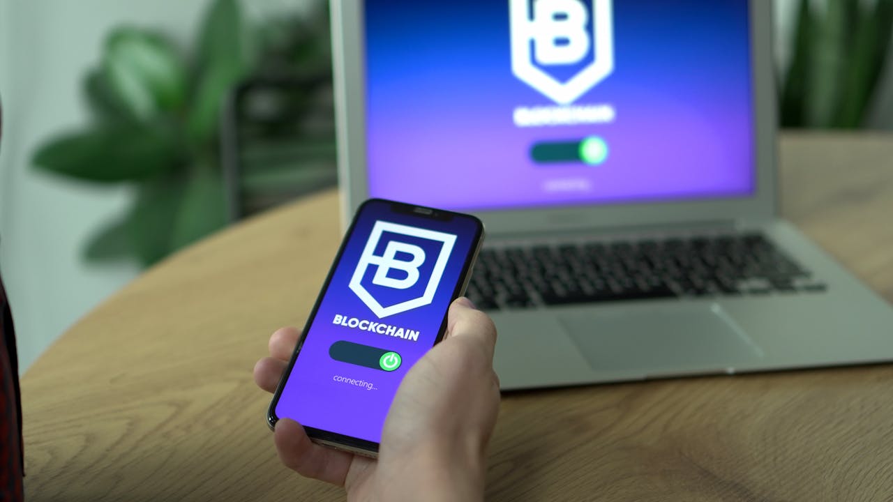 Features Person uses a blockchain application on smartphone, mirrored on laptop screen.